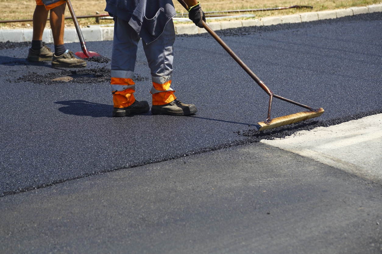 Manual workers helping to level the asphalt surface for a steamroller to press.